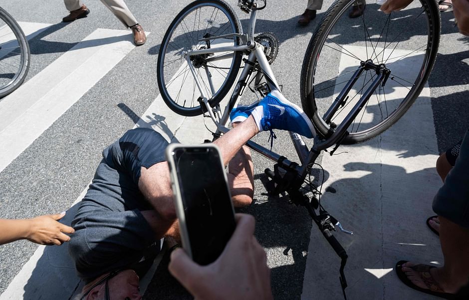 US president Joe Biden falls off his bicycle as he approaches well-wishers following a bike ride at Gordon's Pond State Park in Rehoboth Beach, Delaware, on 18 June 2022.