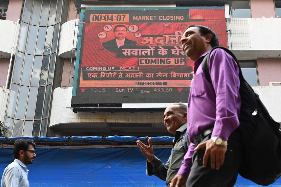 People walk past an electronic signage displaying news on the Adani Group at the Bombay Stock Exchange (BSE) building in Mumbai on 27 January, 2023