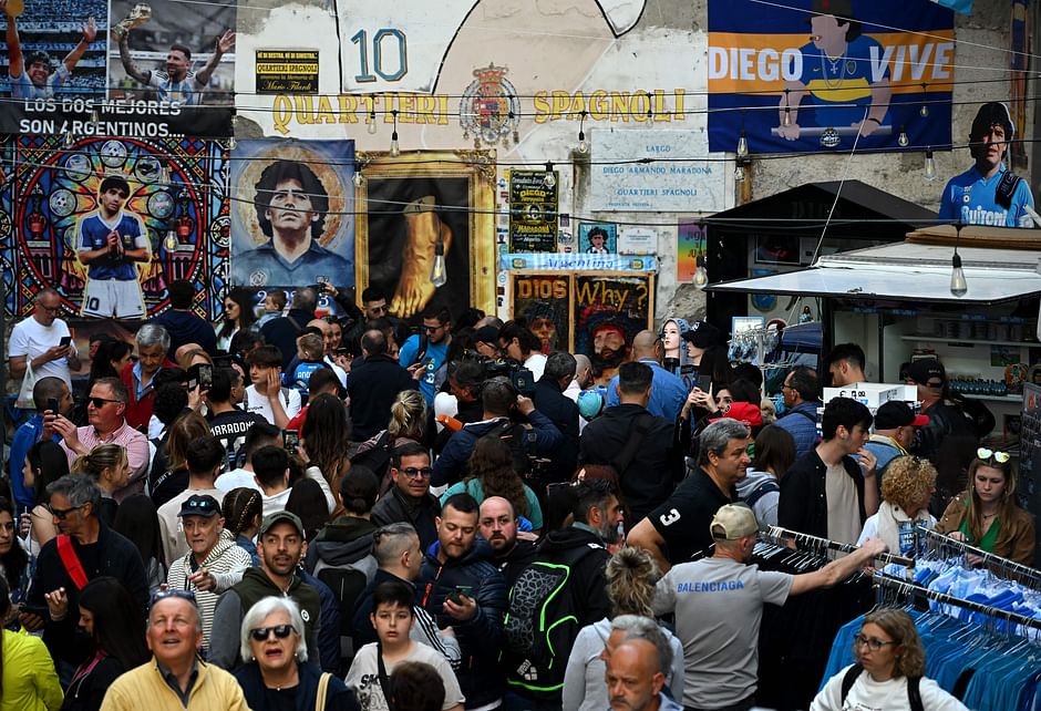 Pedestrians walk past a graffiti depicting Argentine's football legend Diego Maradona, with flags, banners and a papier mache model of Naples's football players, in the colors of Napoli, decorating the Quartieri Spagnoli in central Naples on 29 April 2023
