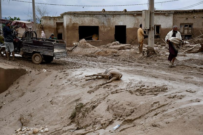 Afghan men walk past the dead body of a donkey along a street covered in mud following flash floods after heavy rainfall at a village in Baghlan-e-Markazi district of Baghlan province on May 11, 2024