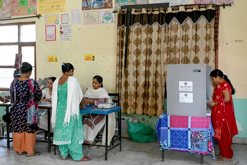 A woman (R) casts her ballot to vote as polling officials verify identity cards of other voters at a polling station on the outskirts of Amritsar on June 1, 2024, during the seventh and final phase of voting in India's general election