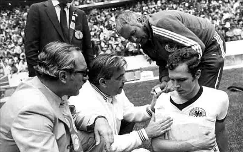 West German defender Franz Beckenbauer (R) gets his right shoulder bandaged by a masseur as the team's doctor Professor Schoberth (L) looks on during the World Cup semifinal soccer match against Italy on 17 June 1970 at Azteca stadium in Mexico City. Photo: AFP