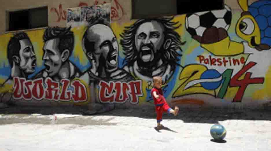 A Palestinian boy kicks a ball in front of graffiti wall murals depicting football players (LtoR) Portugal