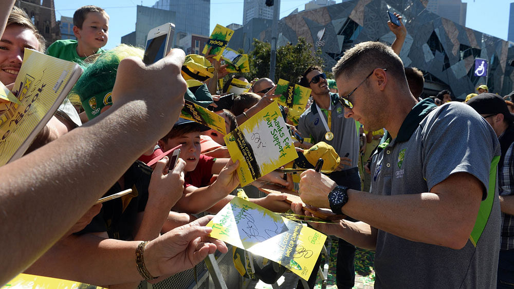 Australian captain Michael Clarke signs autographs as teammate Mitchell Johnson obliges a fan with a selfie during a public event to celebrate their victory in the world cup in Melbourne on March 30, 2015. Photo : AFP