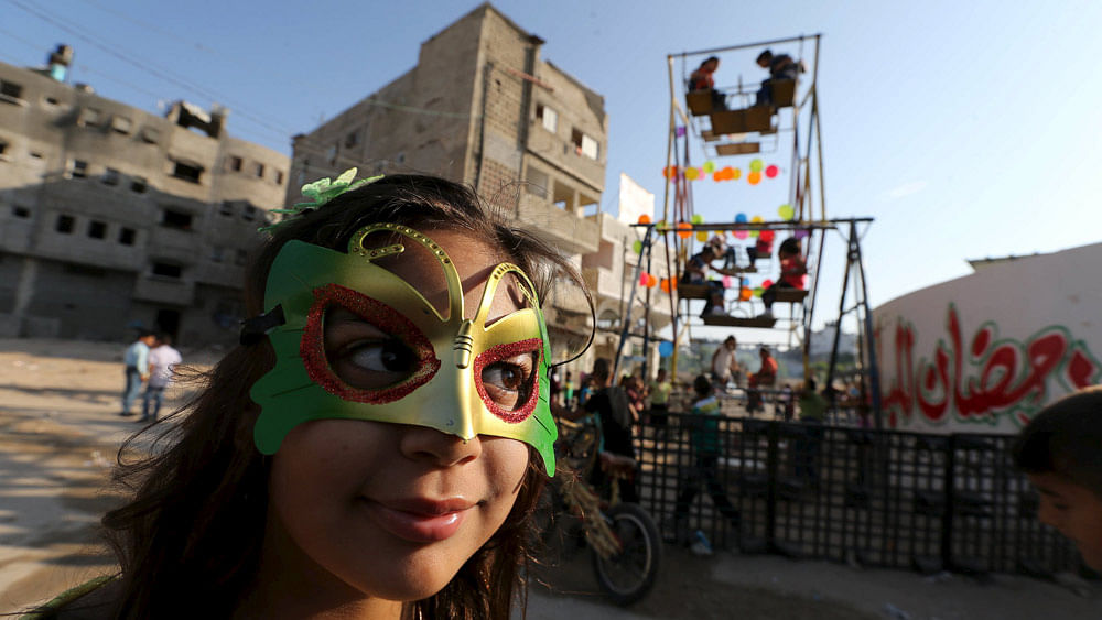 A Palestinian girl wears a mask as children enjoy a ride on a ferris wheels on the first day of Eid al-Fitr holiday, marking the end of the holy month of Ramadan, in the east of Gaza City, July 17, 2015.Photo: Reuters