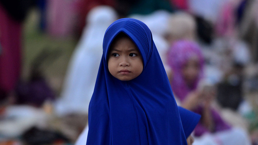 A young girl looks on as Muslim people offer special morning prayers near the Bajra Sandhi monument in Denpasar on Bali island on July 17, 2015. Photo: AFP