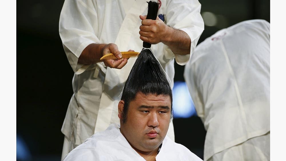 A specialist hairdresser demonstrates the unique topknot sumo wrestler hairstyle on an athlete, during a presentation by professional sumo stables promoting the sport, at a department store in Tokyo August 29, 2015. Photo: Reuters