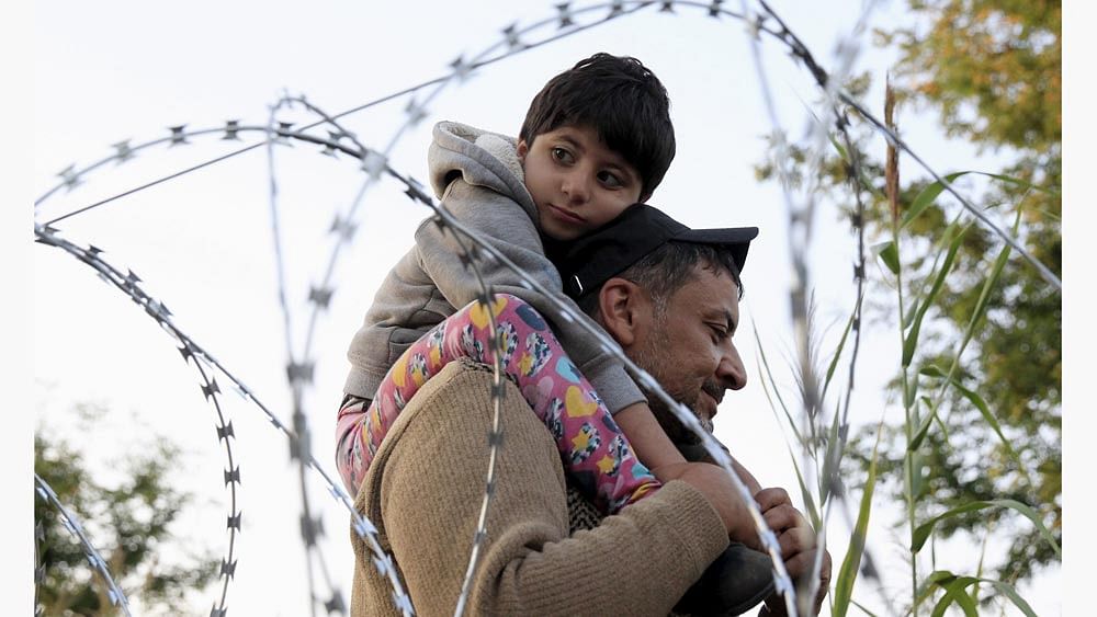 A Syrian migrant with a boy, on the Serbian side of the border with Hungary, walks behind a razor wire near Roszke, Hungary August 28, 2015. Photo: Reuters