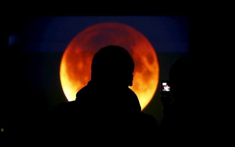 People look at the screen displaying the moon, appearing in a dim red colour, which is covered by the Earth`s shadow during a total lunar eclipse in Warsaw, Poland September 28, 2015. Photo: Reuters