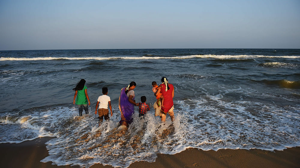 Indian women Sindhu (R) and her sister Muthu Lakshmi (C) hold the hands of their children as they play at the waters edge in the late afternoon in the beach in Chennai on 15 March 2016.  Photo: AFP