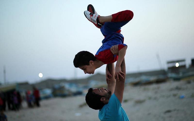 Palestinian boy Mohamad al-Sheikh, 12, who is nicknamed `Spiderman` and hopes to break the Guinness world records with his bizarre feats of contortion, is held by his trainer as he demonstrates acrobatics skills on a beach in Gaza City June 2, 2016. Photo: Reuters