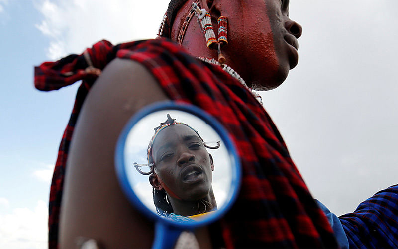 A Maasai moran athlete is reflected in a grooming mirror as he smears his colleague`s face with red ocher paint during preparations for the 2016 Maasai Olympics at the Sidai Oleng Wildlife Sanctuary, at the base of Mt. Kilimanjaro, near the Kenya-Tanzania border in Kimana, Kajiado, Kenya December 10, 2016. Photo:Reuters