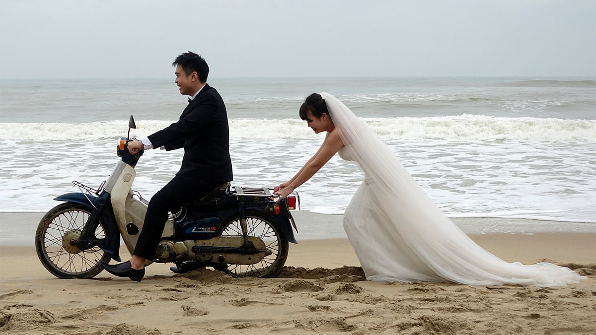 A Vietnamese bride is seen pushing the groom on a scooter during a photo shoot for their wedding in An Bang Beach outside Hoi An in Vietnam December 11, 2016. Photo: Reuters