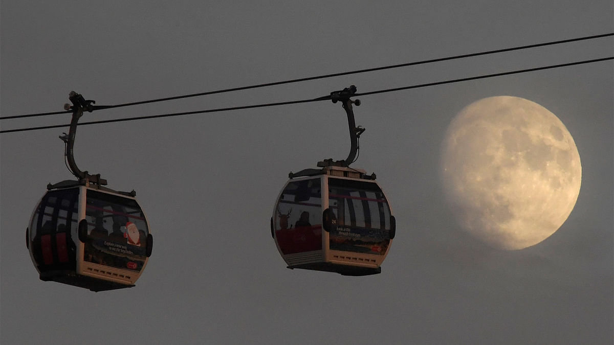 Passengers cross the River Thames in cable cars with the moon seen behind at Greenwich Peninsula in London, Britain December 11, 2016. Photo: Reuters