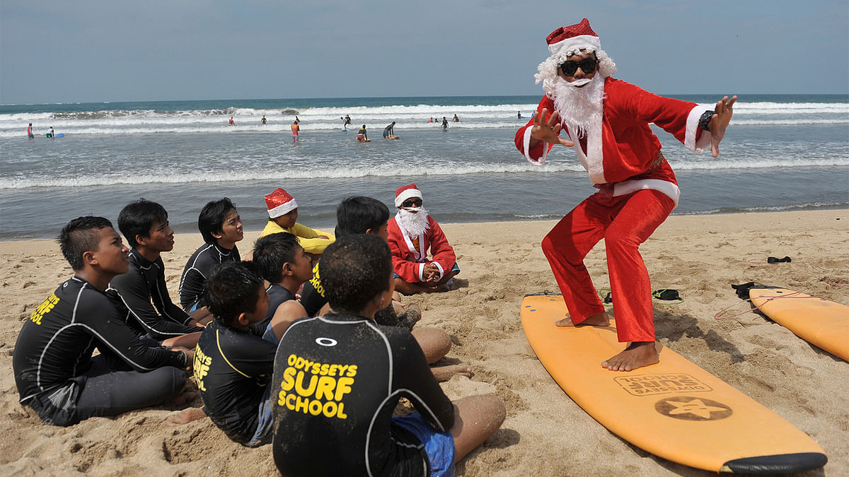 A surfing instructor dressed as Santa Claus gives a lesson to orphans on Kuta Beach. Photo: Reuters