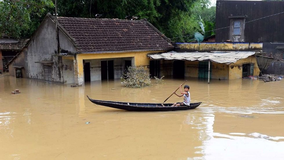 A boy paddling a boat past flooded houses in the central province of Binh Dinh on 19 December, 2016. Photo: AFP