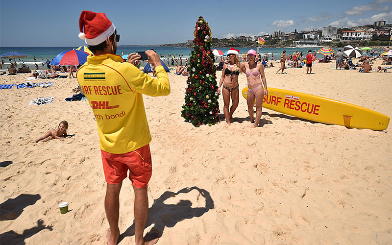 A surf lifesaver takes a photo for visitors (C) posing next to a Christmas tree on Bondi Beach to mark Christmas Day in Sydney on December 25, 2016. Photo: AFP