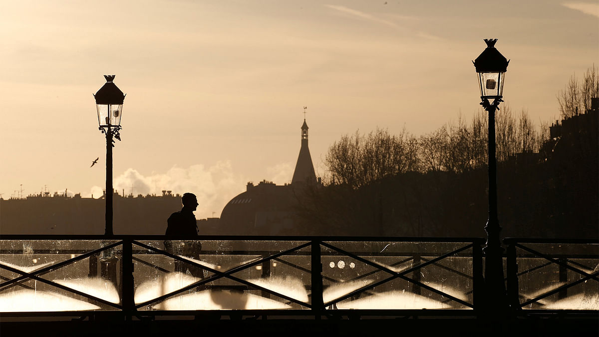 A man walks on the Pont des Arts bridge as the sun rises above the Seine River skyline in central Paris, France December 28, 2016. Photo: Reuters
