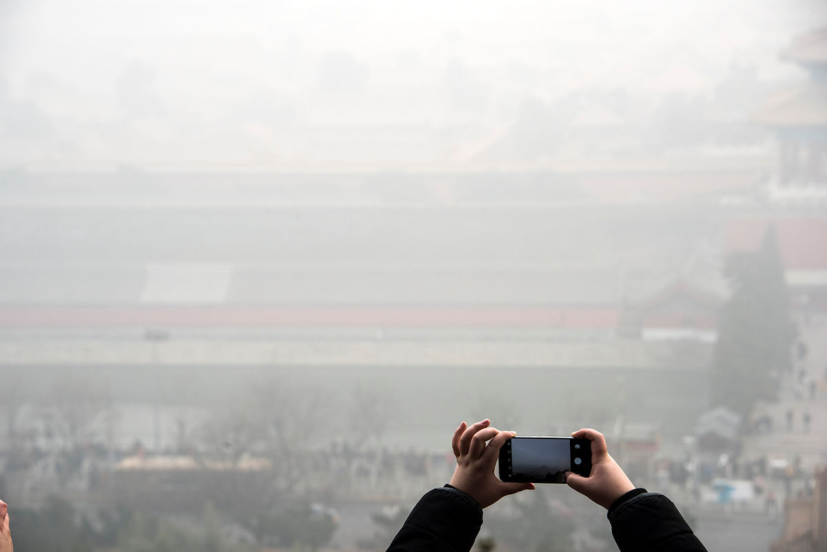 A person takes pictures with a mobile phone of city scenery during a hazy day in Beijing. AFP