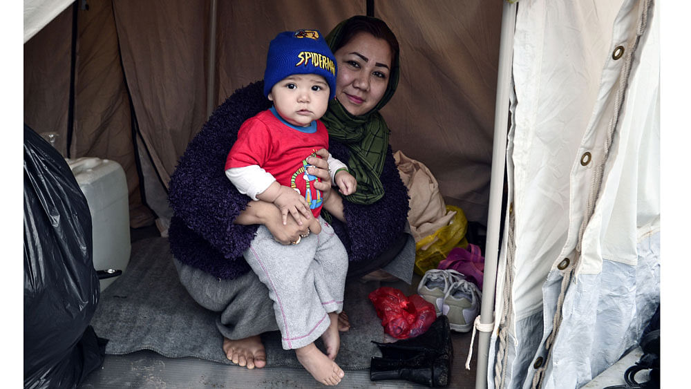 An Afghani refugee woman and mother of three poses with one of her children in their tent set up on a baseball field at a refugee camp in the Hellinikon Olympic Complex, in a southern Athens suburb, on January 11, 2017. AFP