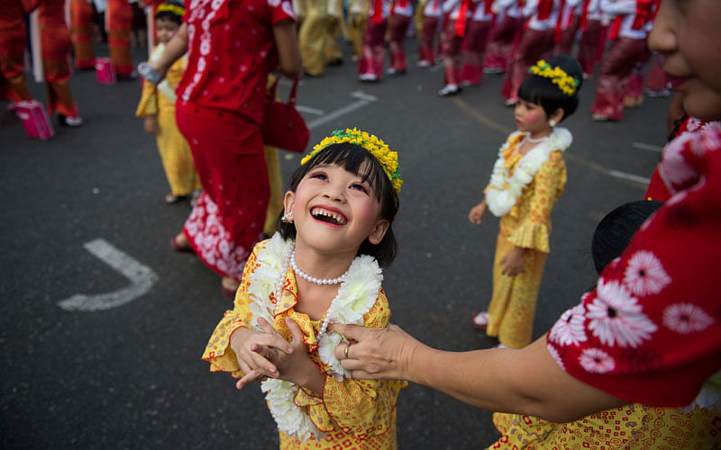 A girl in a traditional dress smiles as she watches a large bunch of balloons rise into the air above City Hall marking the beginning of the Buddhist New Year or `Thingyan` as it is known locally on April 13, 2017 in Yangon.Photo: AFP
