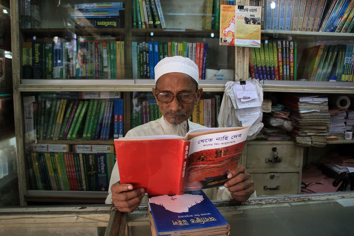 In this photograph taken on April 17, 2017, Bangladeshi novelist Kasem bin Abubakar poses for a photograph with a copy of one of his books at his book shop in Dhaka. Photo: AFP