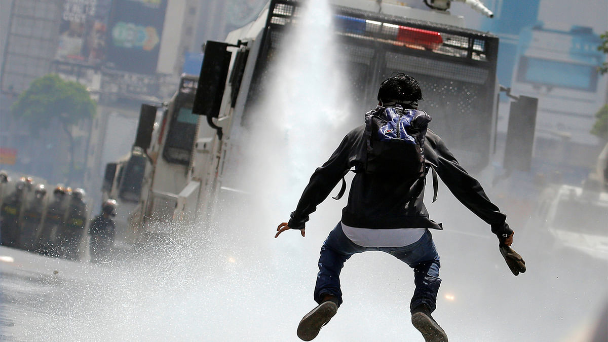 A demonstrator jumps away from a jet of water released from a riot security forces vehicle during a rally against Venezuela`s President Nicolas Maduro in Caracas, Venezuela, May 26, 2017. Photo: Reuters