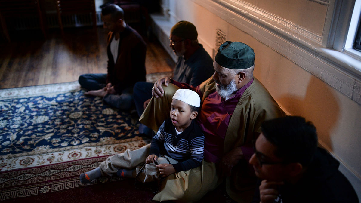 A boy sits on the lap of a Muslim man and he and others recite prayers ahead of the Maghrib sunset prayer at a Sufi service during the month of Ramadan in Manhattan, New York, U.S., on June 3, 2017. REUTERS