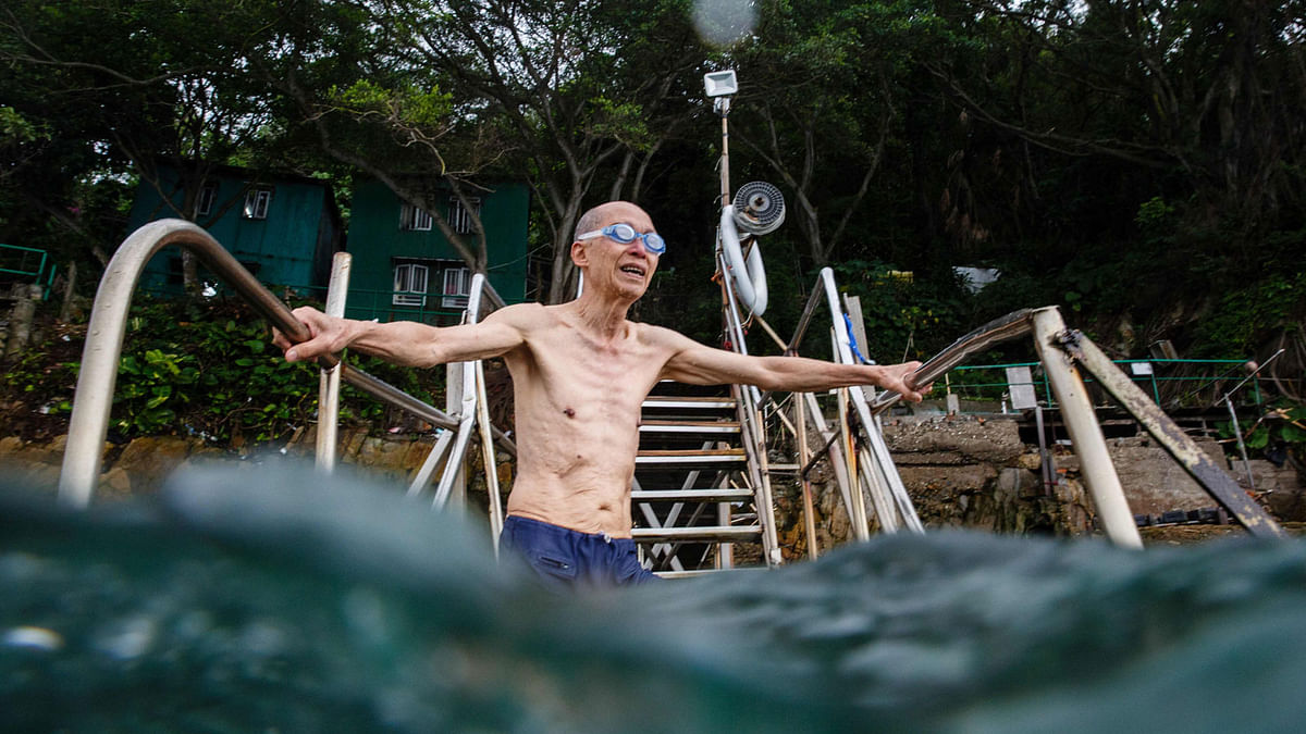 In this picture taken on June 2, 2017, an elderly man stands on the steps of a wooden pier as he prepares to swim below the `Sai Wan swimming shed` (top) off the western tip of Hong Kong Island. AFP
