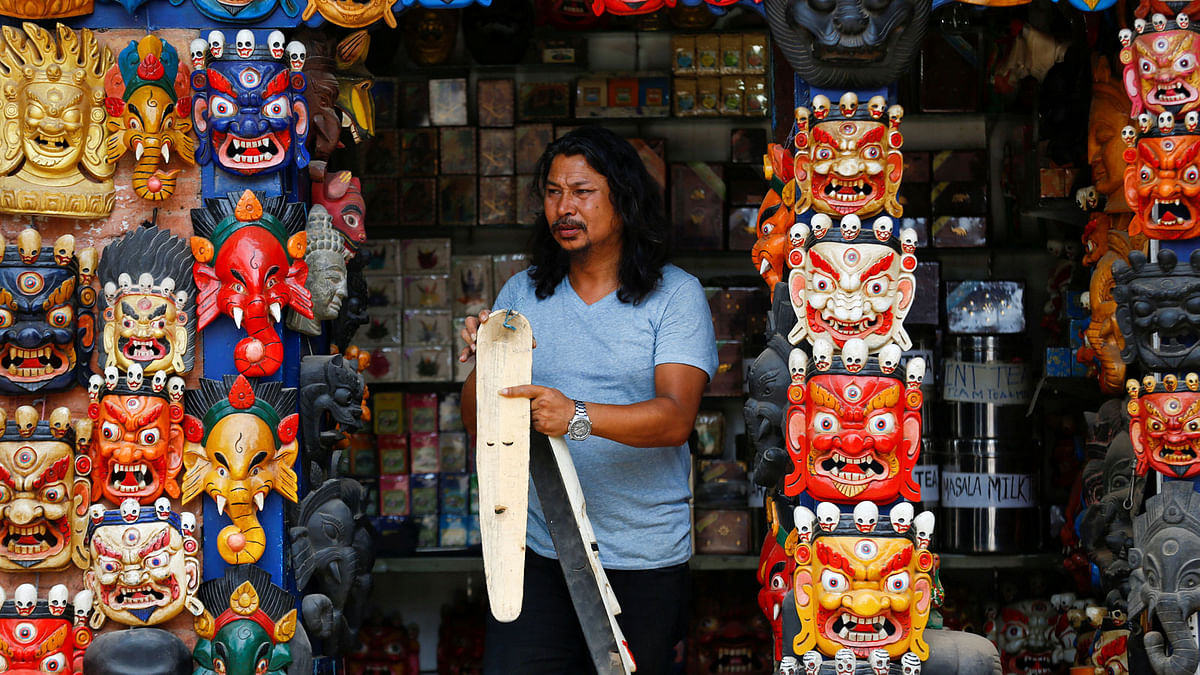 A shopkeeper walks out holding a mask from his souvenir shop in Bhaktapur, Nepal 1 August. Photo: Reuters