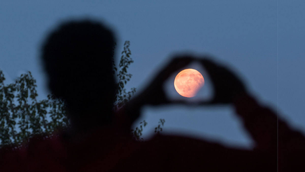A man frames with his hands the moon standing in a partial lunar eclipse on August 7, 2017 in Frankfurt am Main, western Germany. AFP