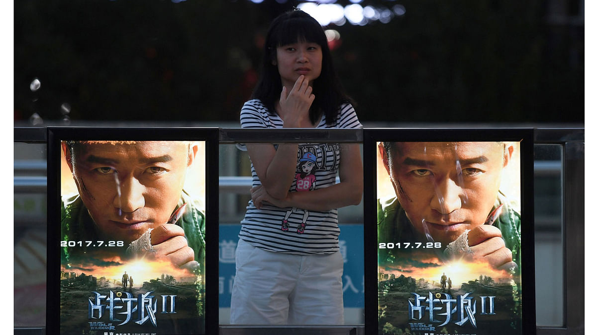 This photo taken on 7 August, 2017 shows a woman standing next to movie posters for `Wolf Warriors 2` in Beijing. Photo: AFP