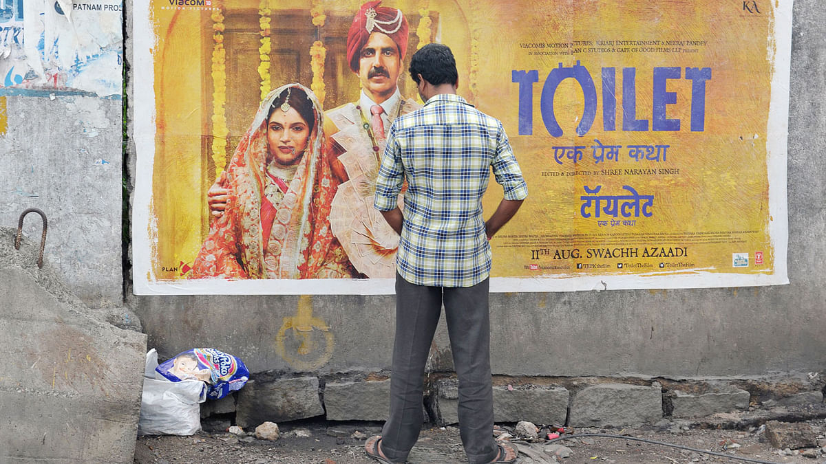 An Indian man urinates on a wall on the roadside in front of a poster for the Hindi film `Toilet` in Hyderabad on 12 August, 2017. Photo: AFP