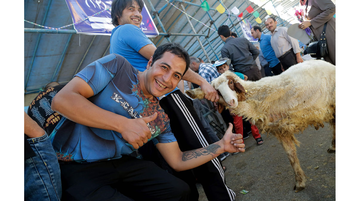 An Iranian man poses with a thumbs-up gesture as another holds the leg of a sheep, at a market in the capital Tehran on September 1, 2017, prior to slaughter as part of the commemoration for the first day of Eid al-Adha. AFP