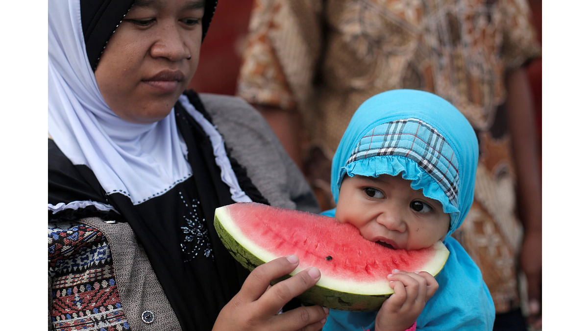 A mother holds her child eating a watermelon during prayers for the Muslim holiday of Eid Al-Adha at Sunda Kelapa port in Jakarta, Indonesia September 1, 2017. Reuters