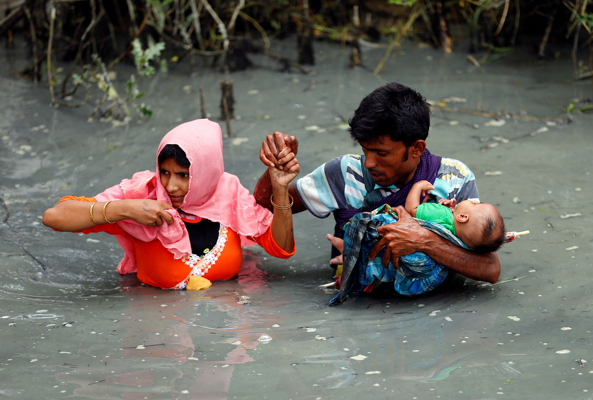Rohingya refugees carry their child as they walk through water after crossing border by boat through the Naf River in Teknaf, Bangladesh on 7 September 2017. Photo: Reuters