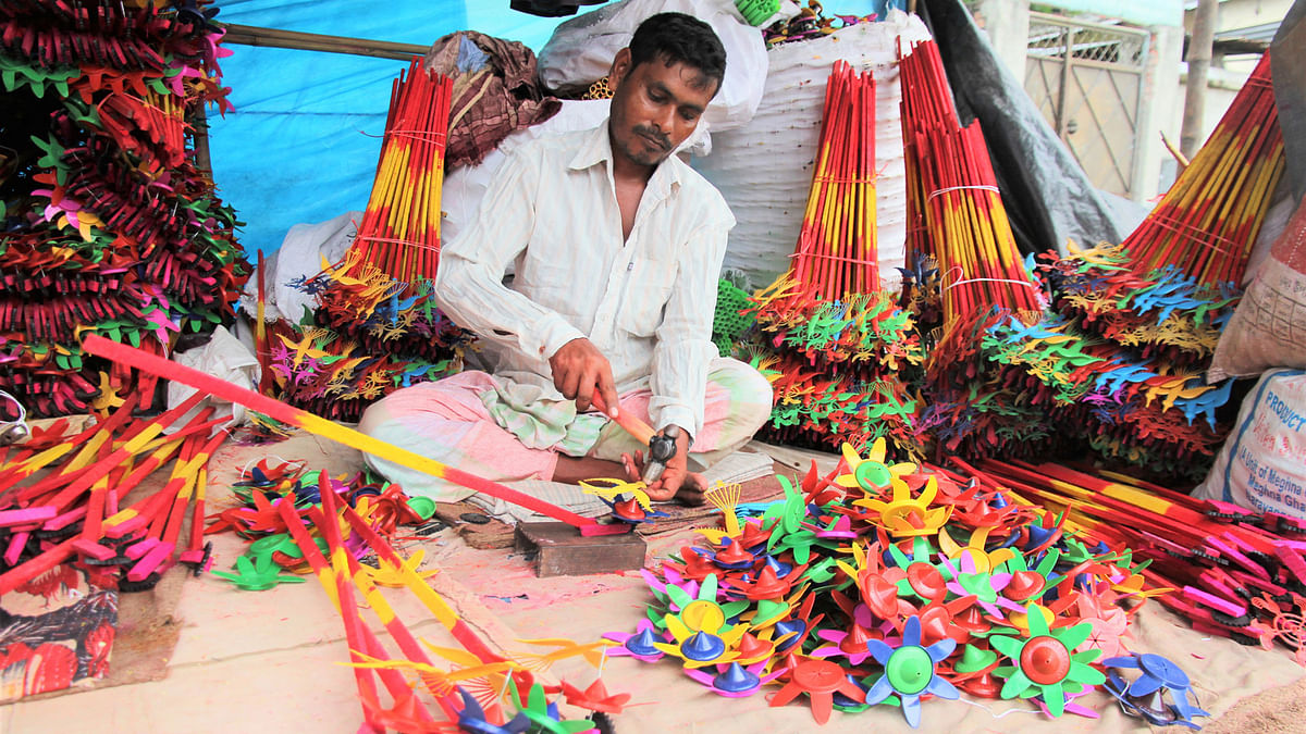 A makeshift toy shop owner works with his products in front of Ram Krishna Asram in Jessore on the eve of Durga Puja on Monday. Photo: Ehsan-Ud-Dawla