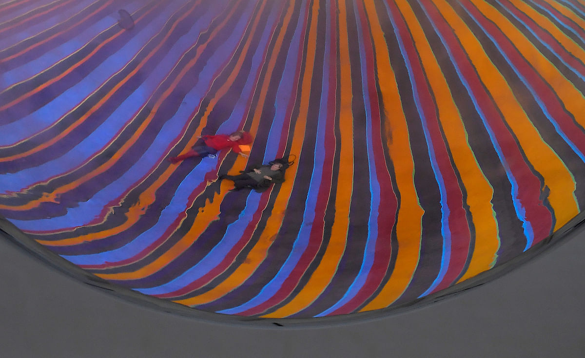 Two visitors are reflected in a silver coloured swinging pendulum as they lie on a huge carpet to view it, which forms part of the new installation `One Two Three Swing!` by Danish art collective SUPERFLEX, at the Tate Modern in London, Britain. Reuters