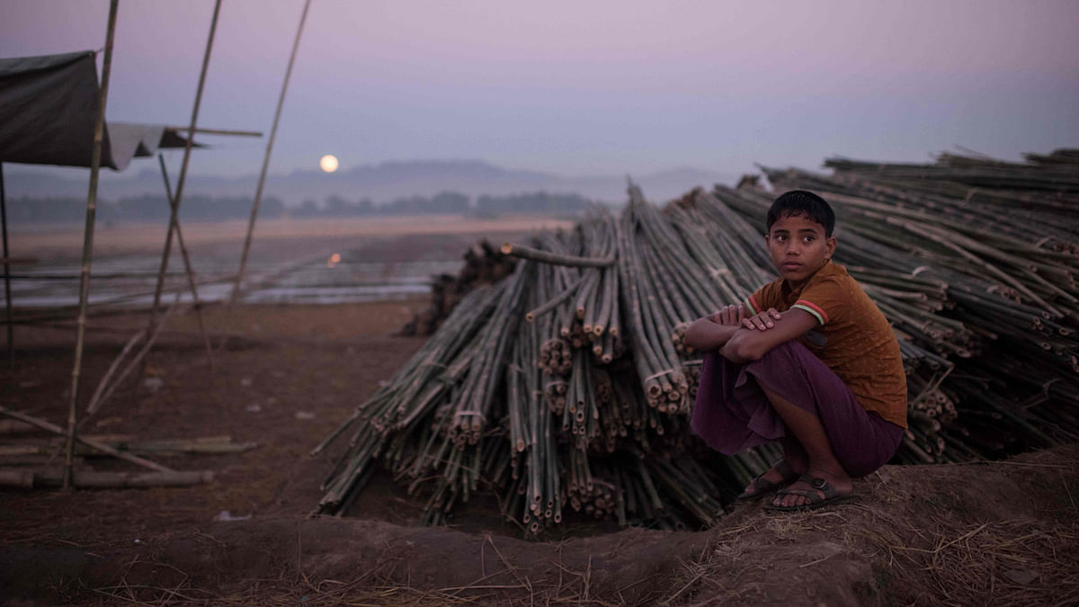 A Rohingya boy sits nest to bamboo used for building sheltes at the Naybara refugee camp, in Cox`s Bazar on 3 December, 2017.  Photo: AFP