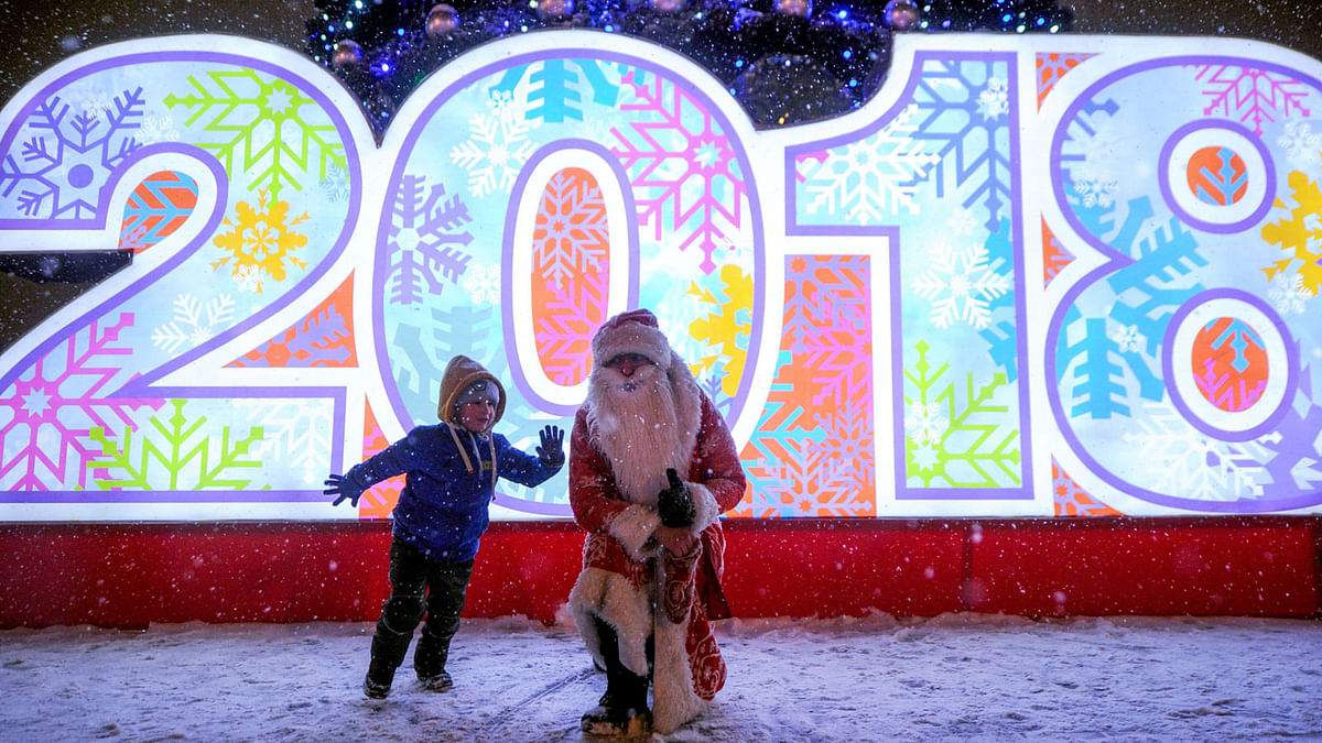 A boy plays with a man dressed as Father Frost in front of a 2018 sign and a Christmas tree in Belarus on 21 December. Photo: AFP