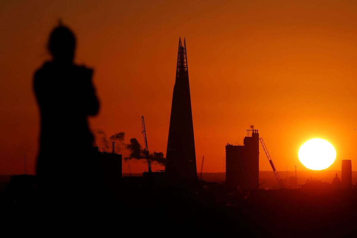 A woman watches the sun rise behind the Shard from Primrose hill in London. Photo: Reuters