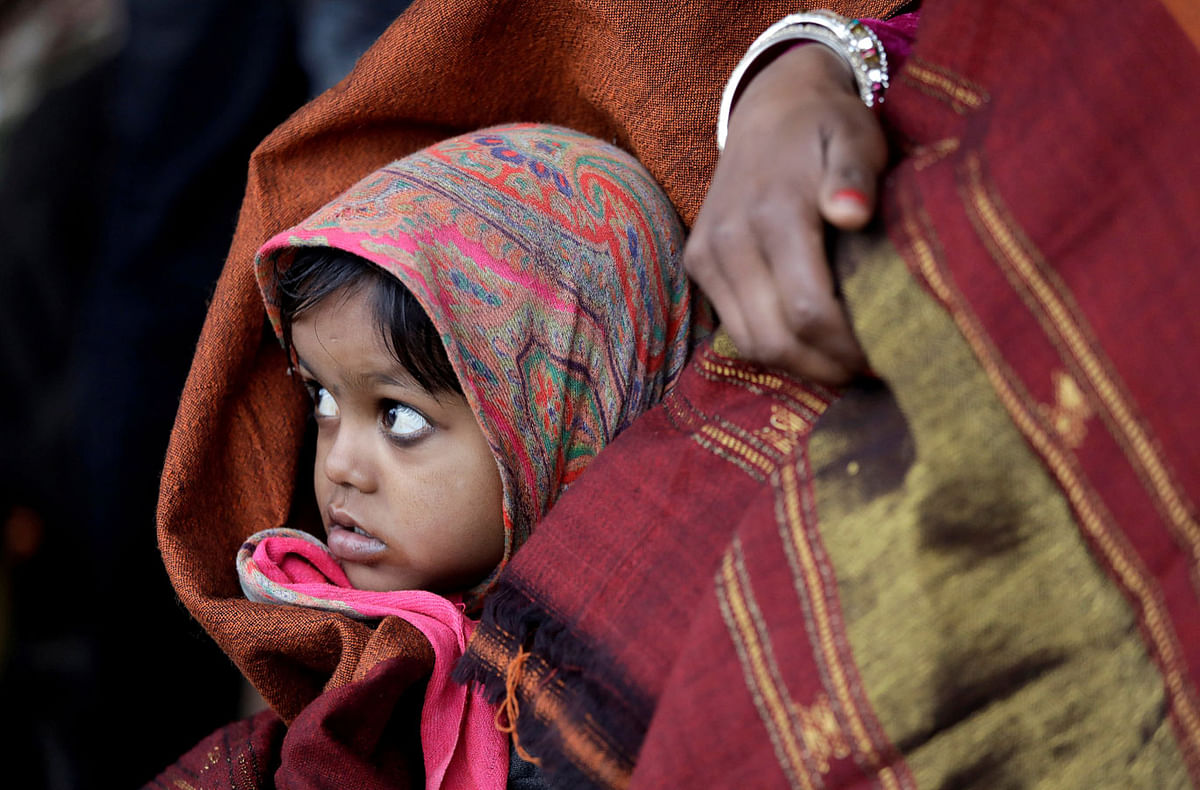 A girl wrapped in a shawl looks on as she waits along with her mother for a train at a railway station on a cold winter morning in New Delhi, India on 3 January 2018. Photo: Reuters