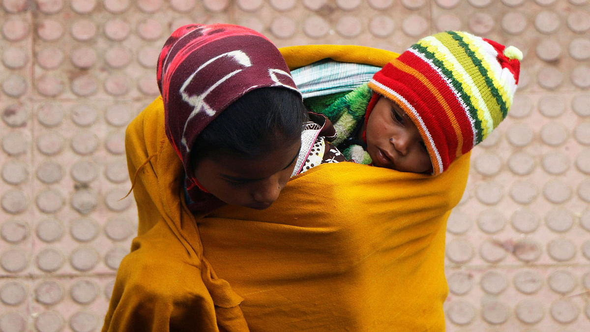 A woman wraps a child in a shawl at a railway station on a foggy winter morning in Agartala, India on 6 January. Photo: Reuters