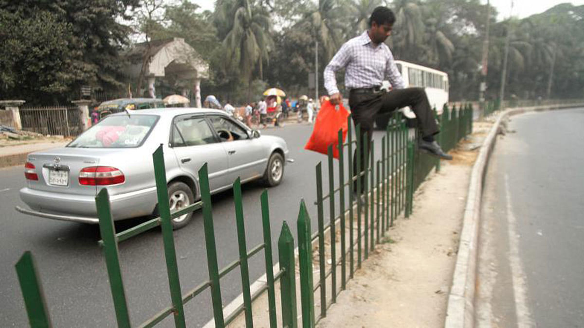 A pedestrian crosses the dangerous road divider in Shishu park area in Dhaka on 2 February 2018. Many people take this risk to save time. Photo: Dipu Malakar