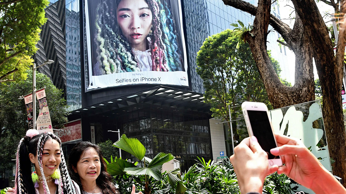 Singaporean designer Kelly Lim (L) poses with a passerby for a photo in front an advertising banner (top) with an image of herself along the Orchard Road shopping district in Singapore on 21 February 2018. Photo: AFP