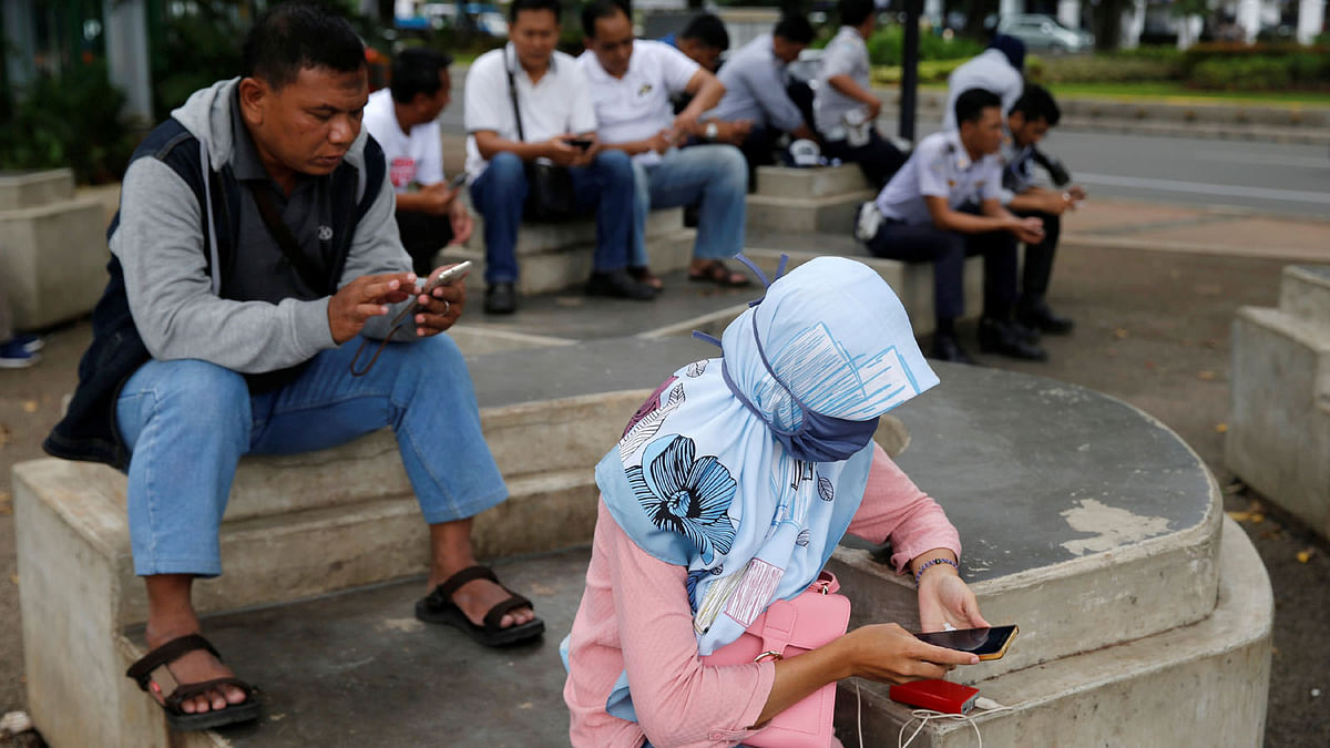 People use smartphones on a sidewalk in Jakarta, Indonesia, on 14 February 2018. Reuters