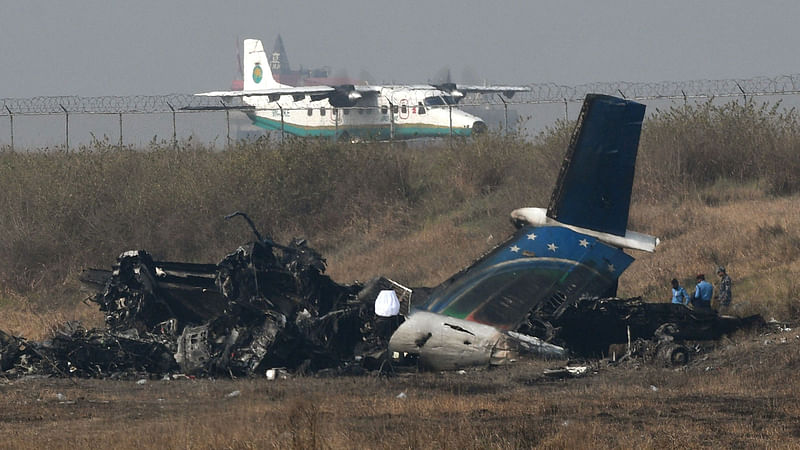 An airplane taxis at the international airport in Kathmandu on  13 March near the wreckage of a US-Bangla Airlines plane that crashed on 12 March . AFP