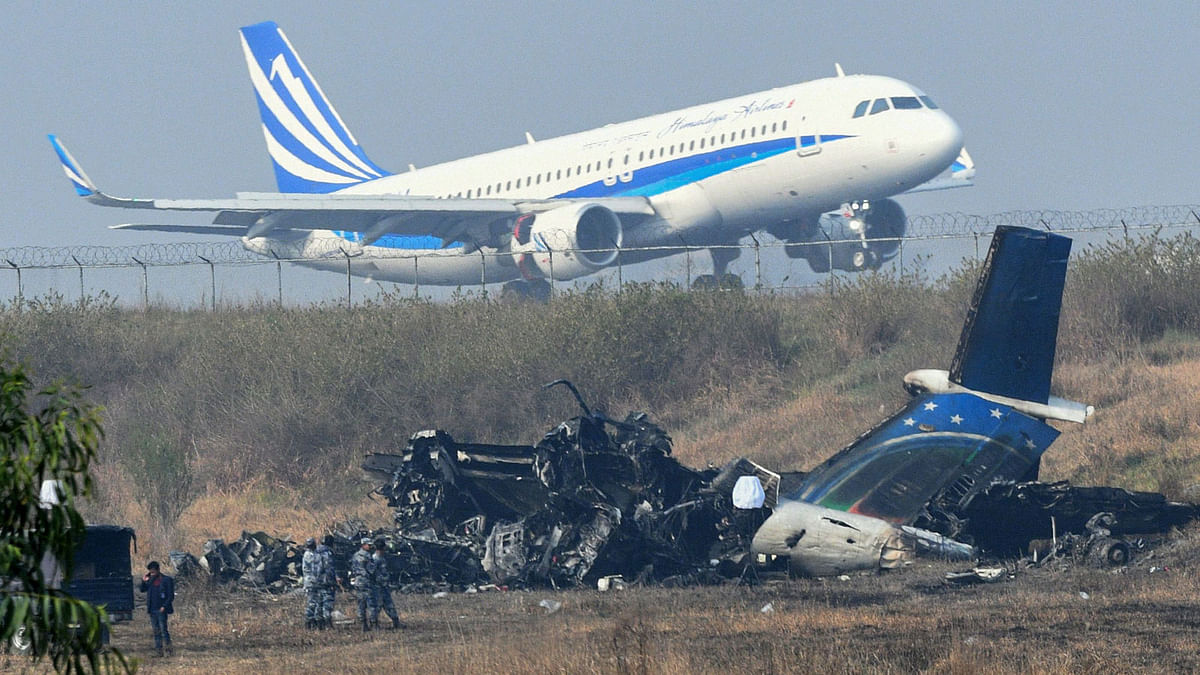 An airplane takes off at the international airport in Kathmandu on 13 March, 2018, near the wreckage of a US-Bangla Airlines plane that crashed on 12 March. Photo: AFP