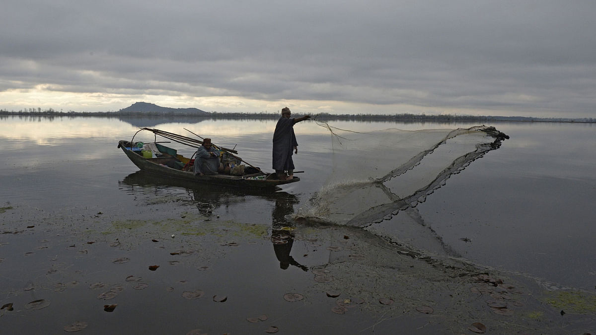 A Kashmiri fisherman casts his net from his boat in Dal lake during cold and rainy day in Srinagar on 14 March. AFP