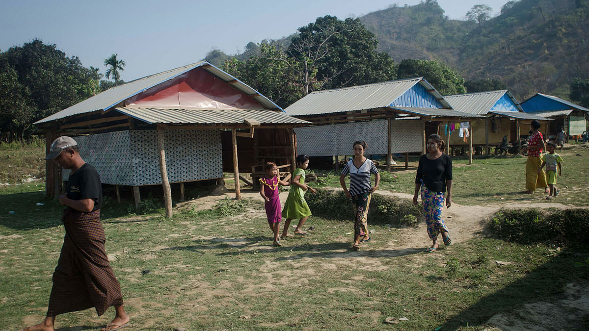 This photo taken on 8 March 2018 shows Rakhine villagers walking past homes in Koe Tan Kauk village, Rathedaung township in Myanmar`s Rakhine State. AFP